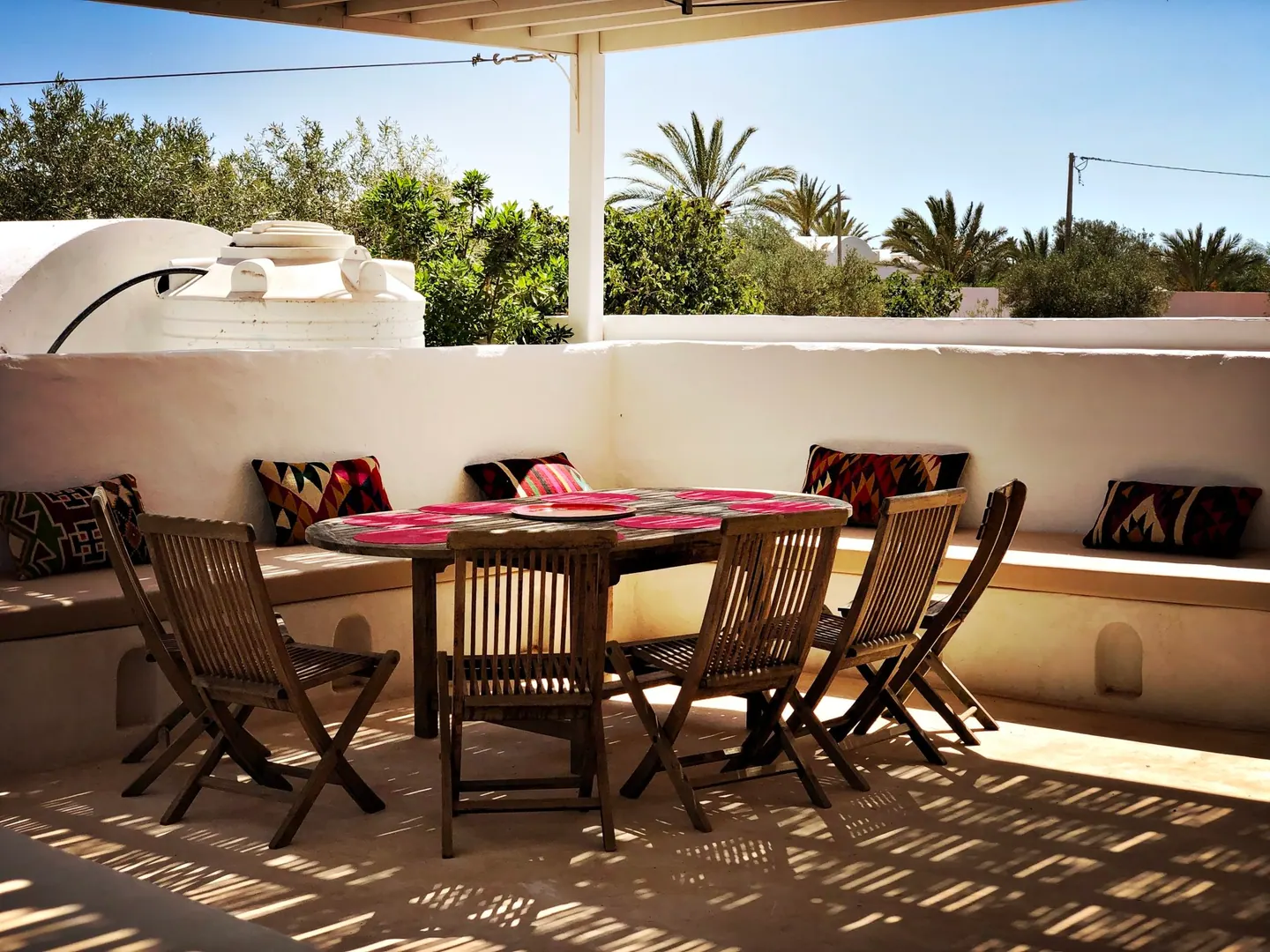 Grande table dressée pour dîner dehors, banquettes maçonnées et coussins
